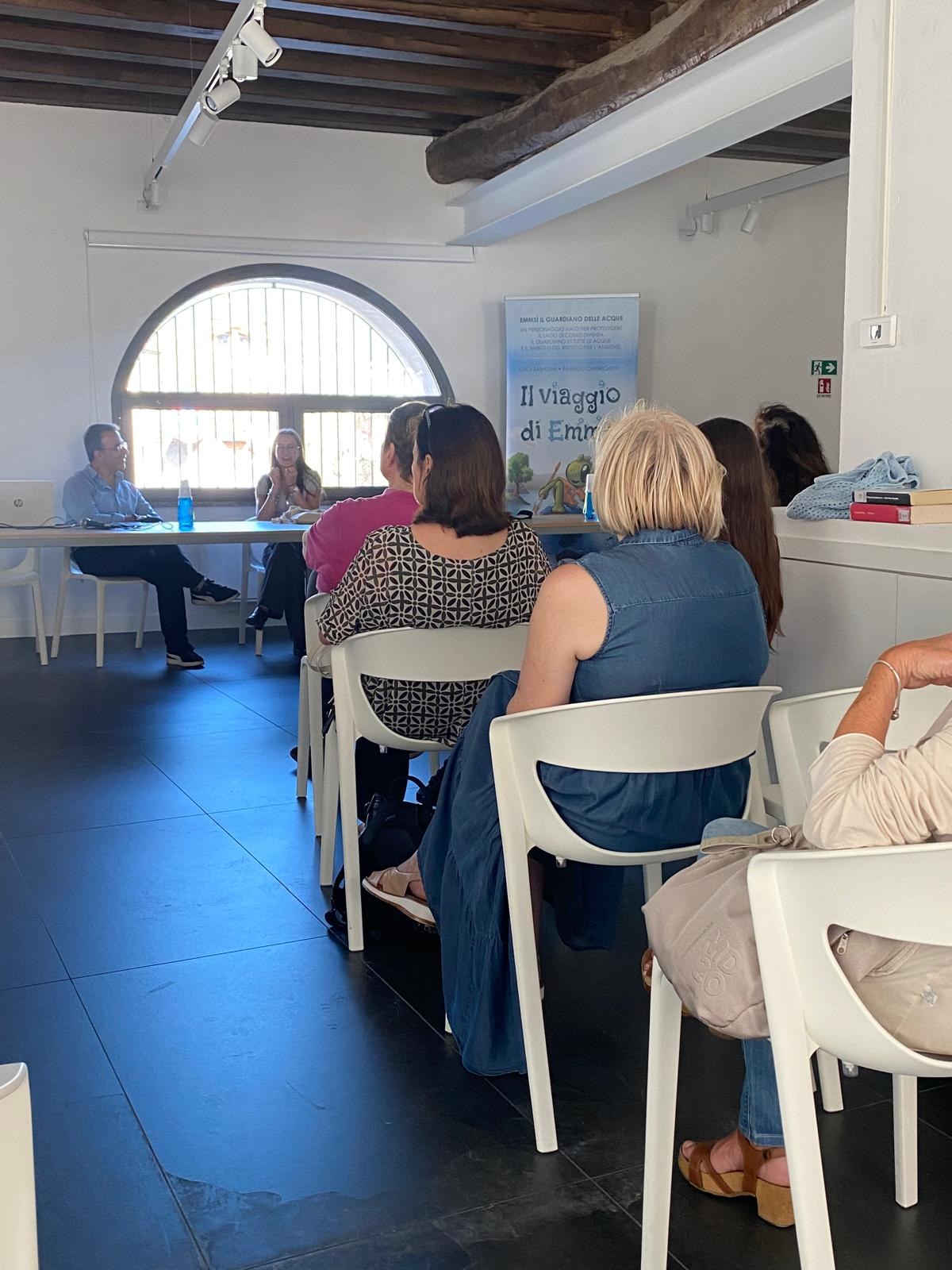 Il pubblico ascolta la presentazione de Il viaggio di Emmsì, sullo sfondo il roll-up del libro